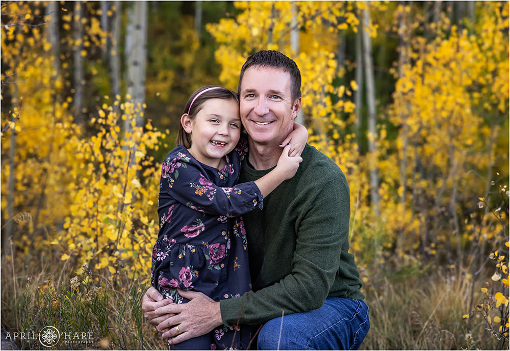 A dad and his young daughter smile as they hug each other at their family portrait in an aspen tree grove in Colorado