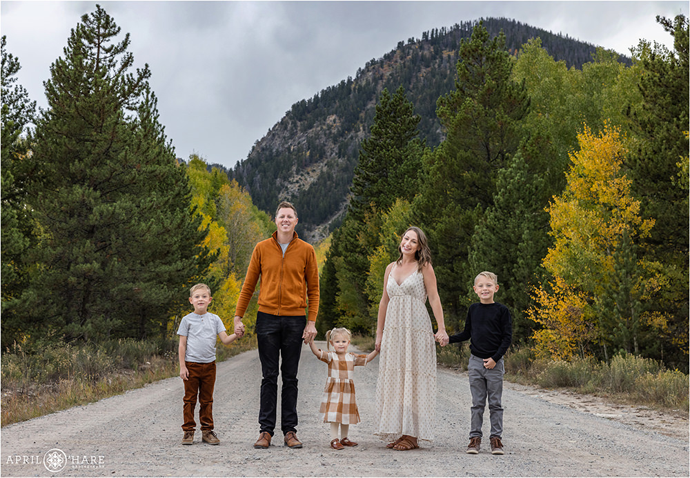 A family of 5 wearing shades of burnt orange pose in the fall color along a dirt road in Summit County Colorado