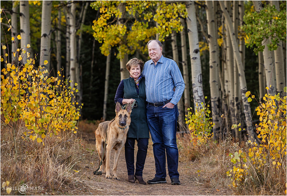 Mom and dad get a photo together with their handsome german shepherd dog in an aspen tree forest in Colorado