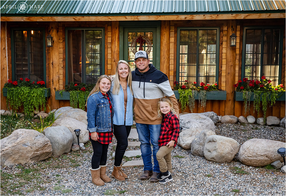 A cute family of four pose for a family picture at a Colorado mountain cabin style home in Grand Lake
