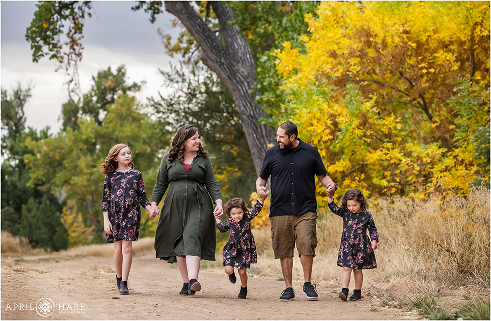 A sweet photo of a family of 5 walking hand in hand with their 3 daughters with a fall color backdrop at James A. Bible Park in Denver