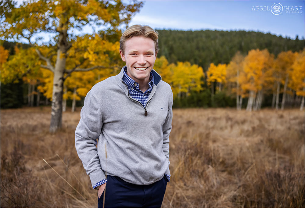 High school senior boy in a mountain meadow full of fall color aspen trees in the backdrop