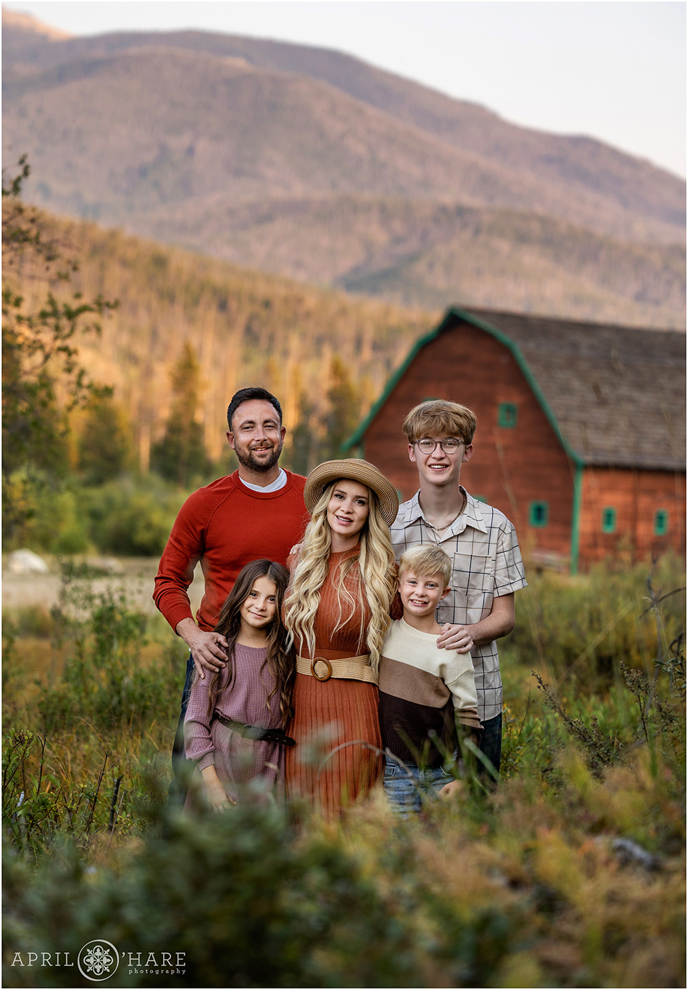 An adorable family of 5 with 3 children pose with a beautiful rustic barn and mountains in the backdrop of Grand Lake Colorado