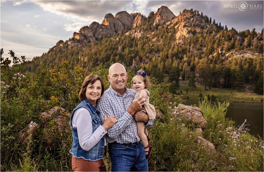 Grandparents get a photo with their young granddaughter with a pretty rocky outcrop in the backdrop at Lily Lake in Estes Park Colorado