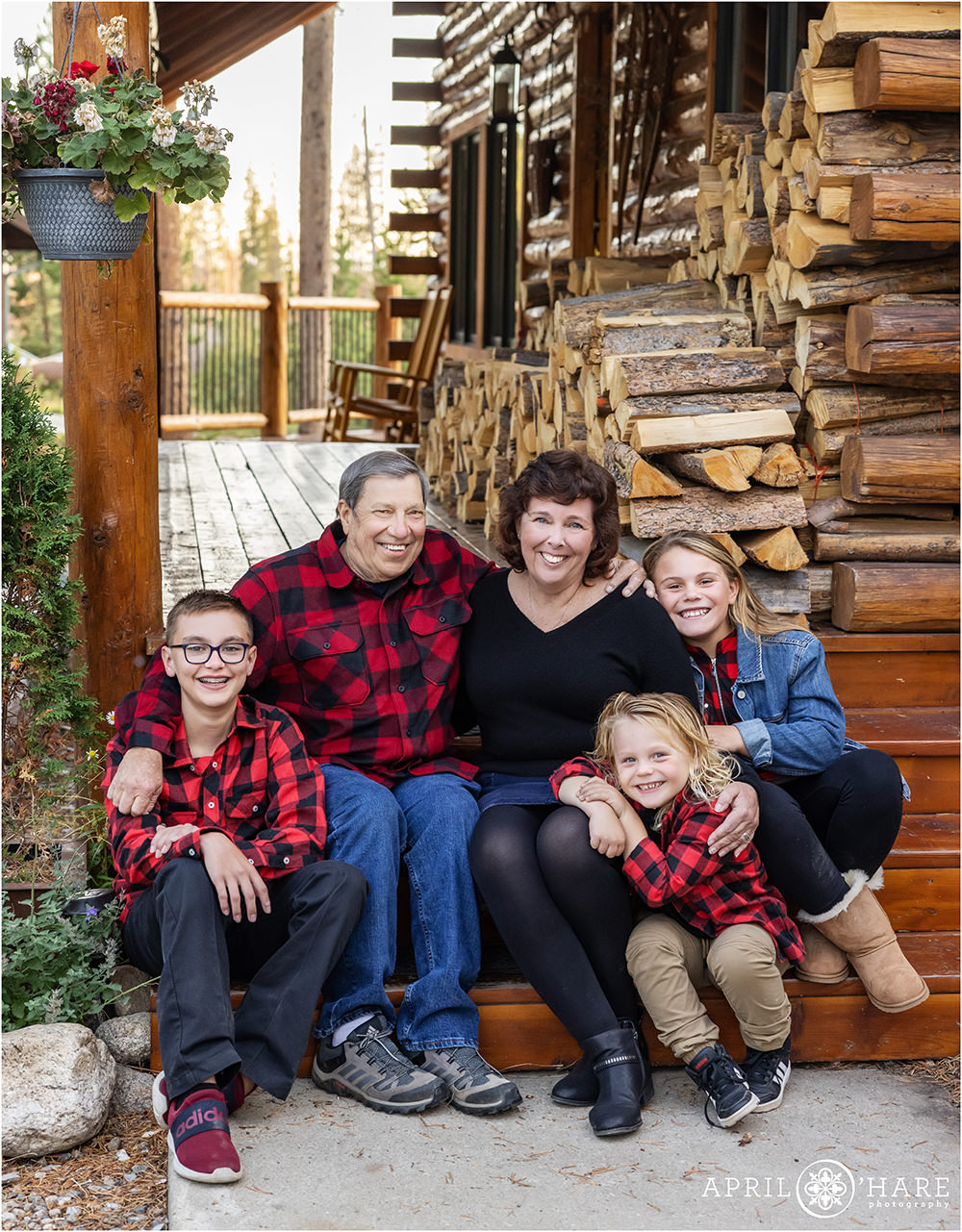 Grandparents sit on front porch area with their grandkids with a pile of wood in the backdrop in Grand Lake Colorado