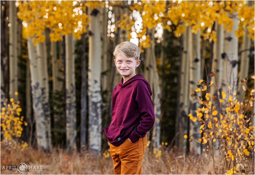 Young boy wearing a maroon top with burnt orange pants in an aspen tree forest in Colorado