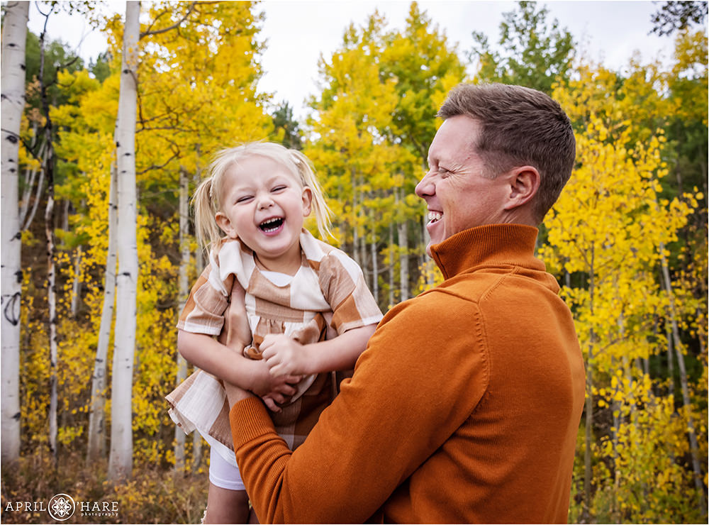 A little girl cracks up laughing with her dad in the golden aspen tree scenery of Colorado