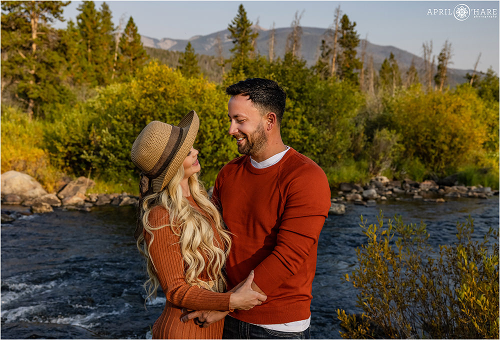 Couple wearing burnt orange clothing pose next to the Colorado River in Grand Lake Colorado
