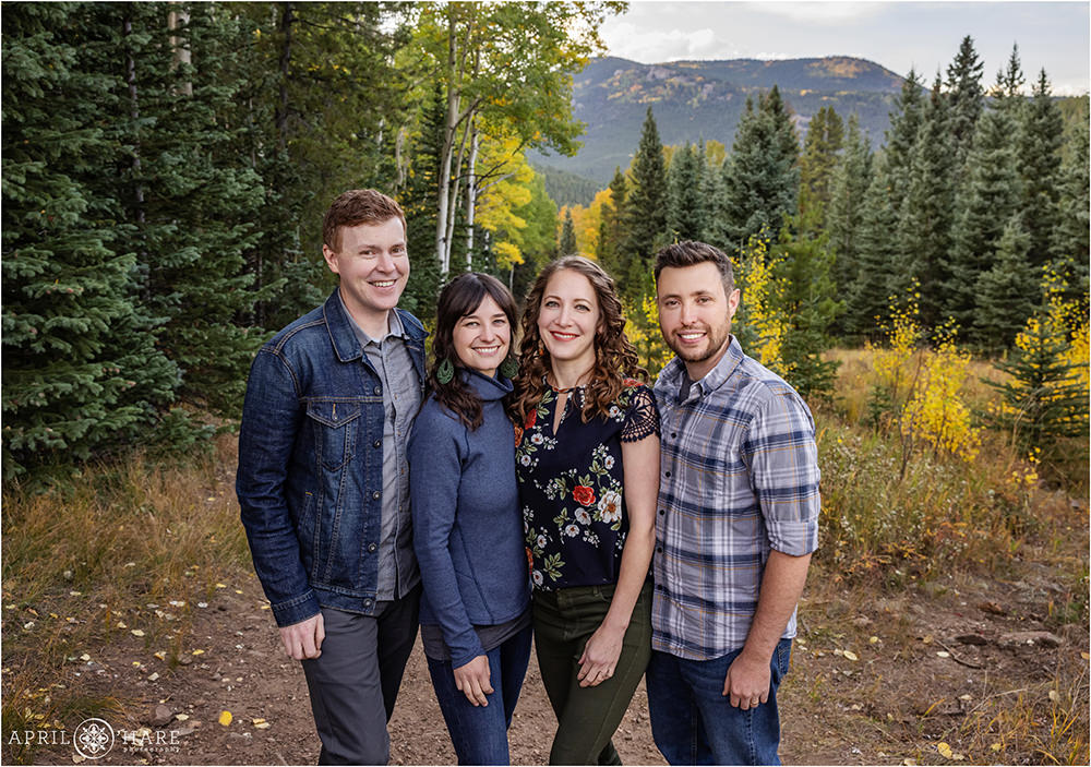 Two brothers and their wives pose for a family photo together with a pretty mounntain backdrop dotted with yellow aspen trees