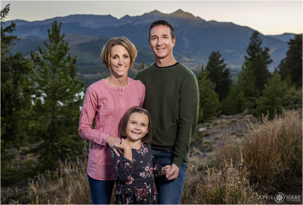 Family of three connected with their hands pose together during fall at Sapphire Point with the mountains in the backdrop