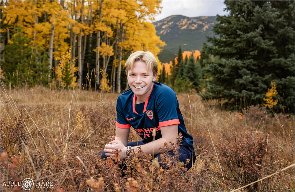 High school soccer player wearing his blue jersey at his senior session in a fall color mountain meadow in Colorado