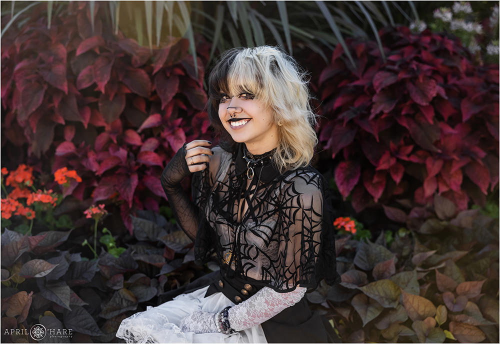 Senior girl with two-toned hair sitting in a dark colored garden setting at Denver Botanic Gardens