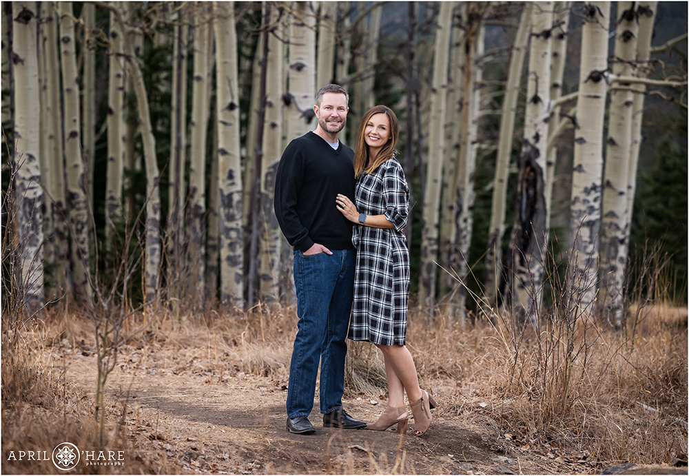 Couple wearing B&W pose in a mountain meadow with aspen tree trunks as their backdrop in Evergreen CO
