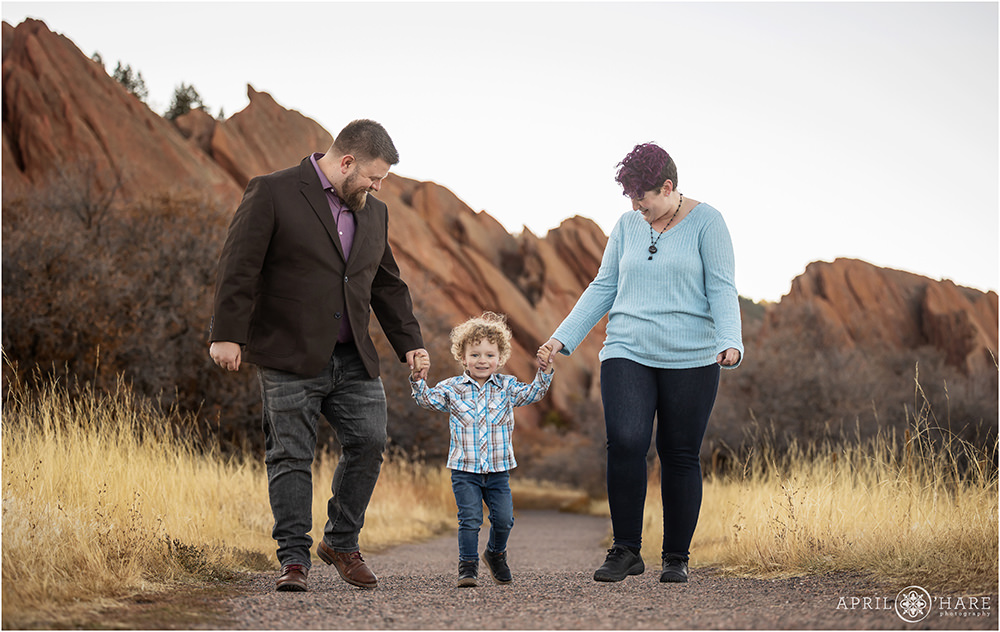 A cute family of three walk down a gravel trail at Roxborough State Park in Colorado