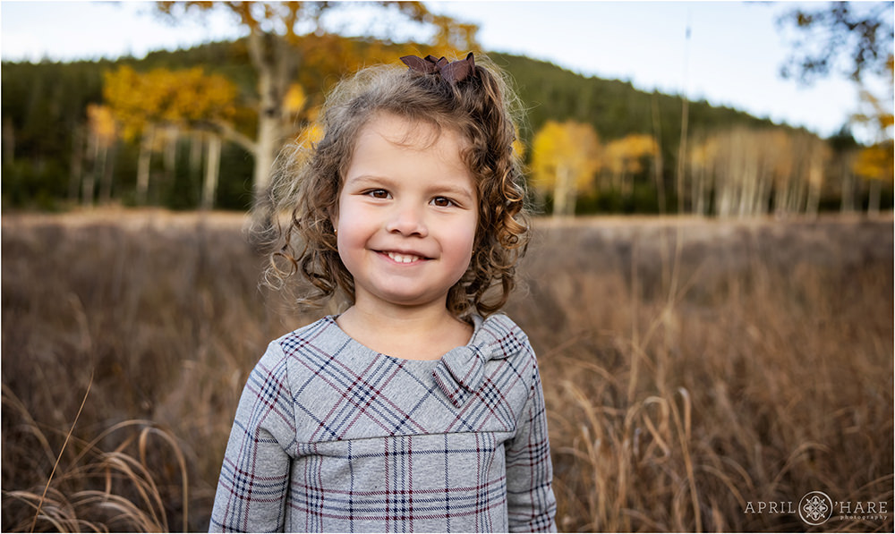 Adorable girl with curly hair stands in a pretty fall color mountain meadow in Colorado