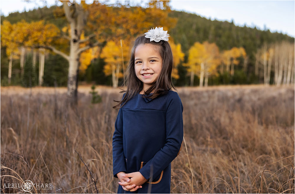 Cute girl wearing a flower bow in her hair and a long sleeved dark blue dress in a pretty fall color mountain meadow in Colorado
