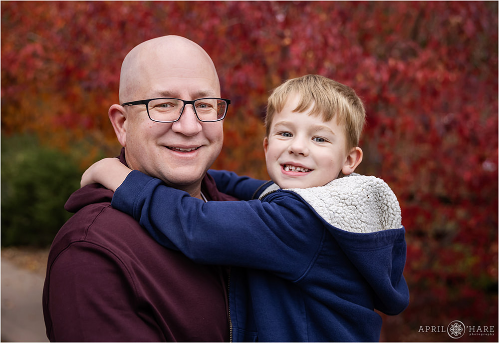 A boy and his dad in front of a pretty bright red autumn tree in Denver
