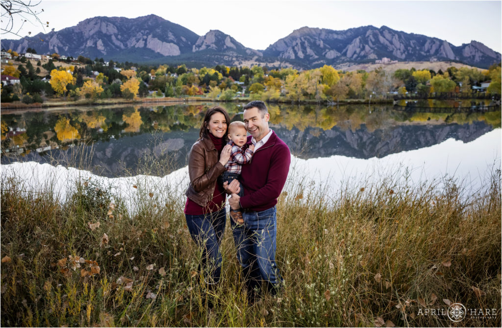 Beautiful fall color portrait of a family of 3 wearing maroon with their adorable baby boy with the fall colors of Viele Lake and the mountains in Boulder in the backdrop