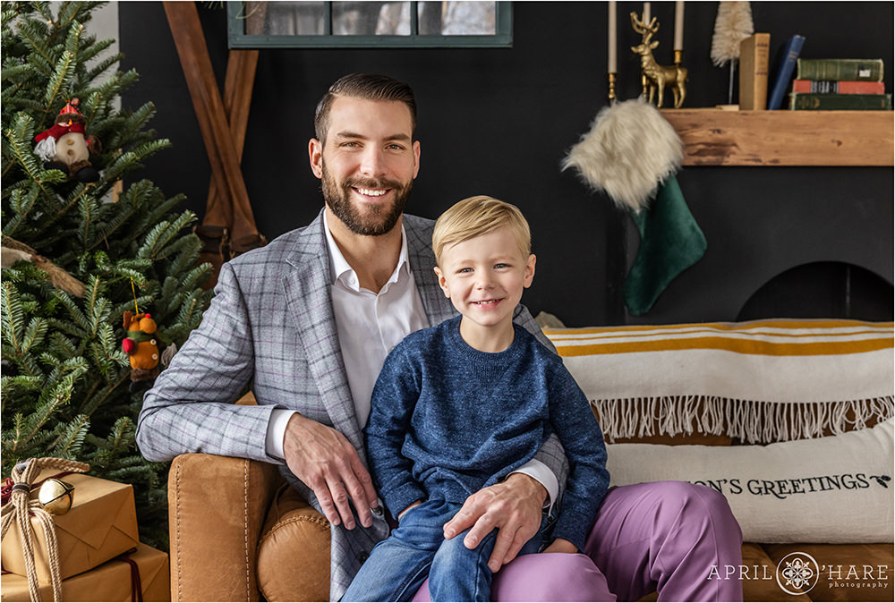 A father and his son pose for a portrait in front of a pretty styled Christmas backdrop in a Denver Photo studio