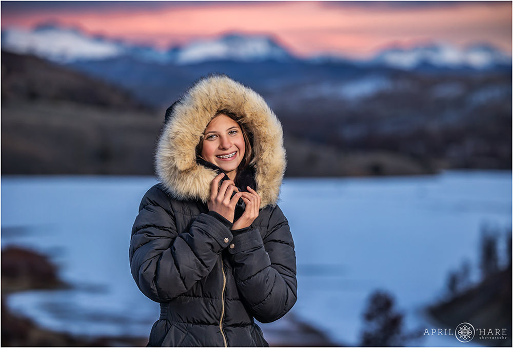 Teen girl wearing a fur lined coat with hood up in front of a pink mountain sunset at C Lazy U Ranch