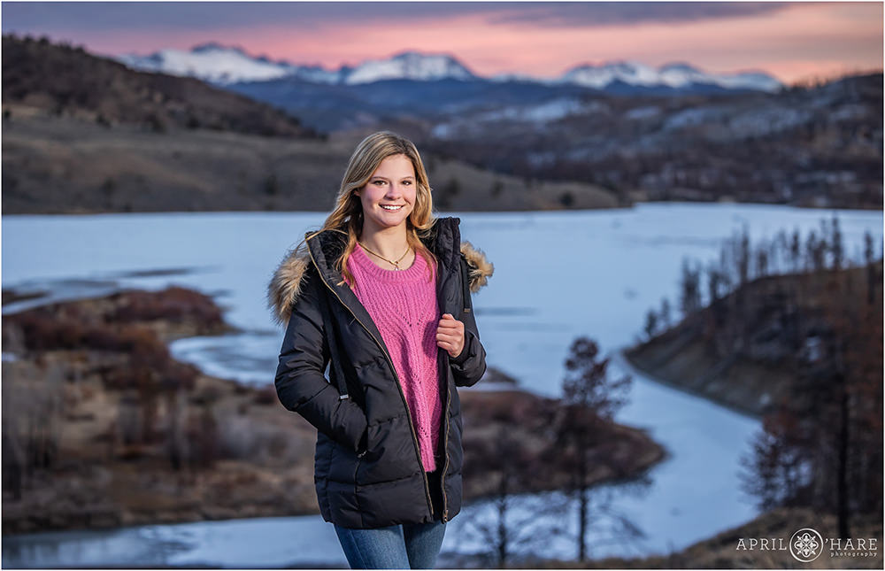 Teenage girl in pink sweather poses in front of pretty sunset mountain backdrop at C Lazy U Ranch in Colorado