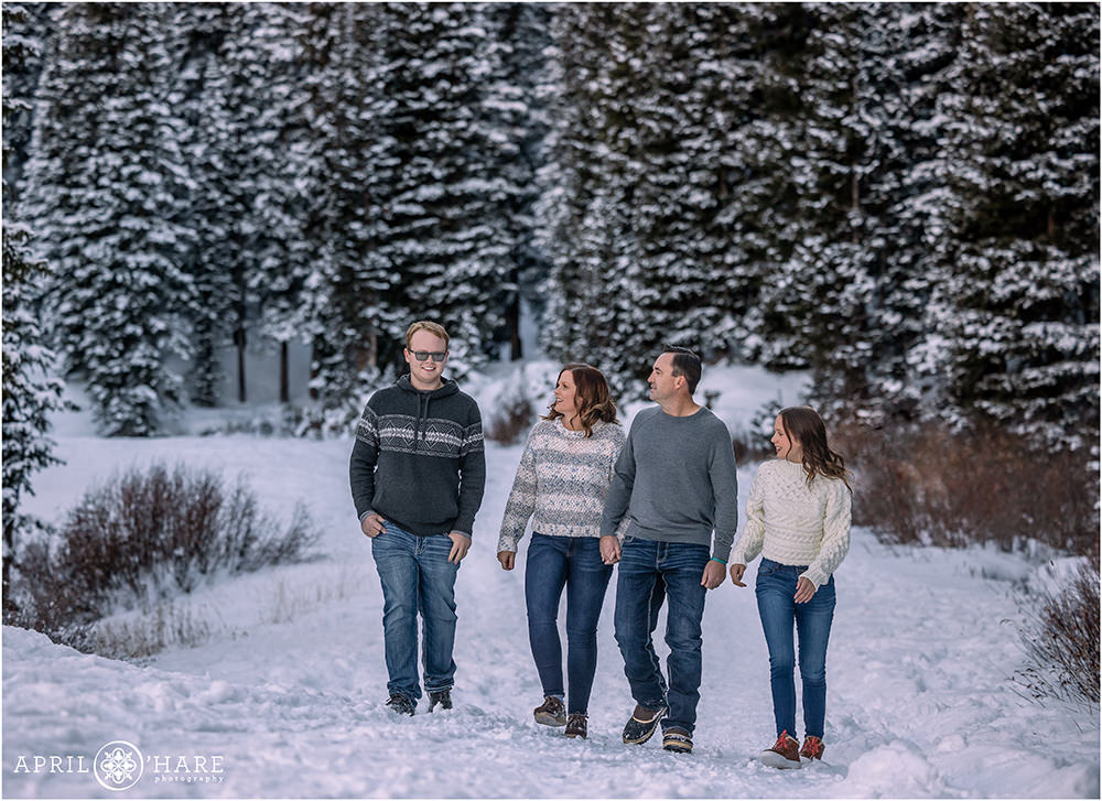Family wearing sweaters and jeans walk through a pretty winter wonderland snow covered forest on their Winter Park family vacation in Colorado