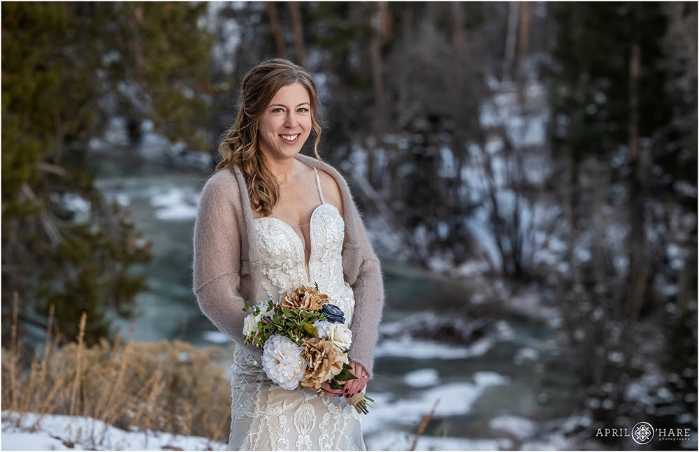 Beautiful bride wearing a cozy shawl posing outdoors during winter in front of the Snake River in Keystone Colorado