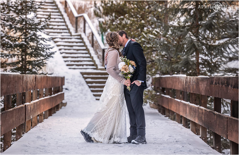 Bride and groom kiss on a snow covered wood footbridge in Keystone Colorado