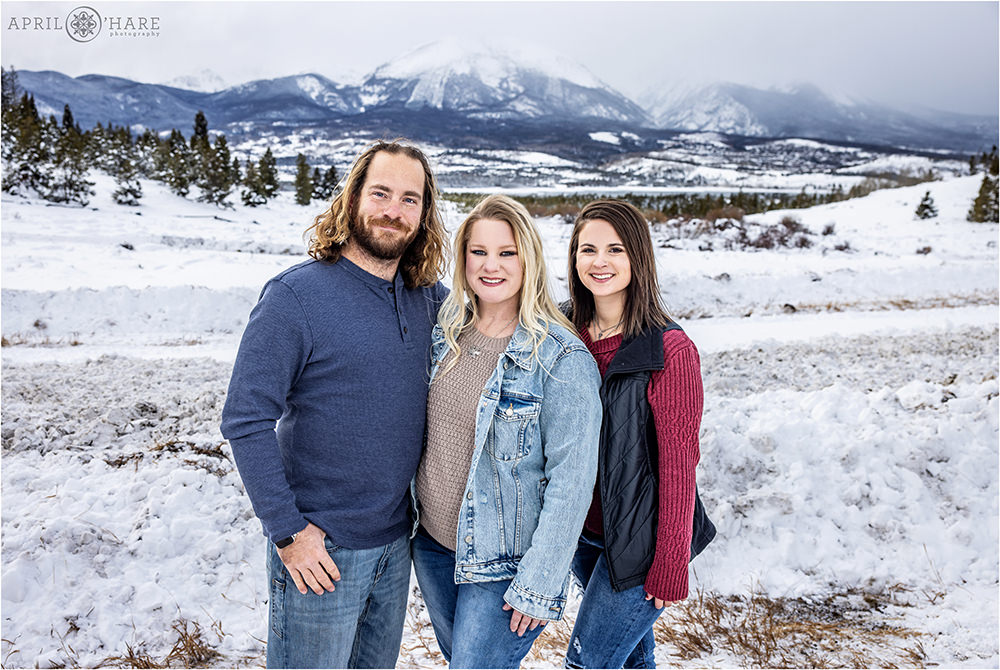 3 adult siblings pose together in the snow with a pretty mountain backdrop in Summit County Colorado
