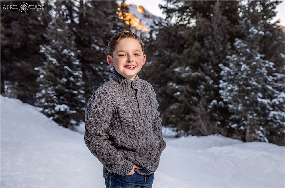 Cute kid wearing a gray sweater is photographed in a beautiful Colorado forest trail with a mountain off in the distance