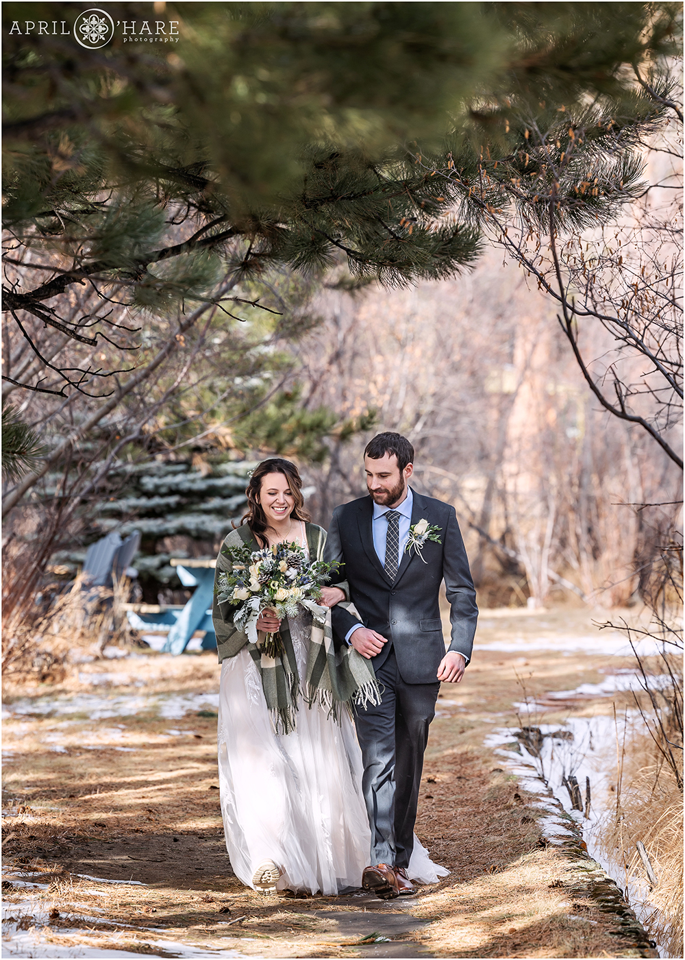 Bride and groom walk down a path to their outdoor winter wedding ceremony at Romantic Riversong Inn in Estes Park