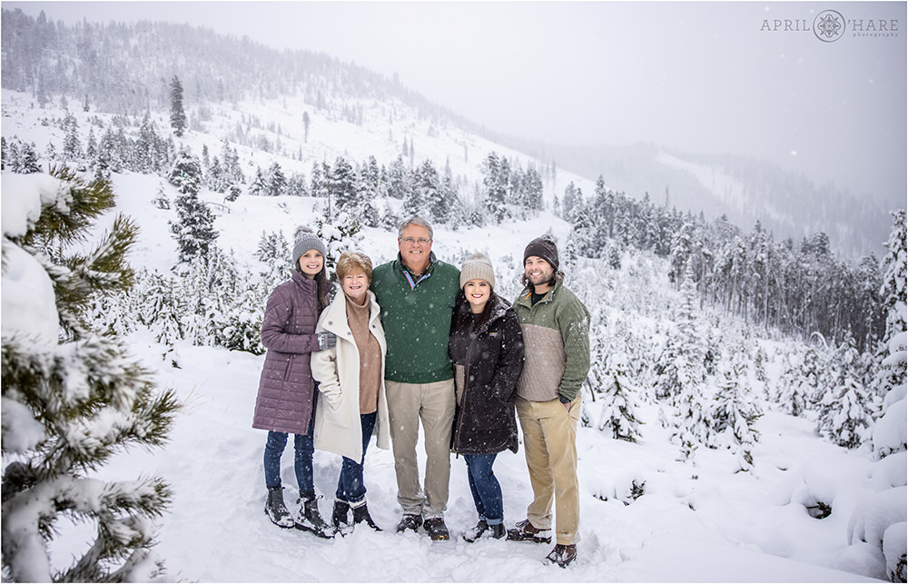 A family of 5 pose in a beautiful winter wonderland setting in the middle of a blizzard style snowstorm in Colorado