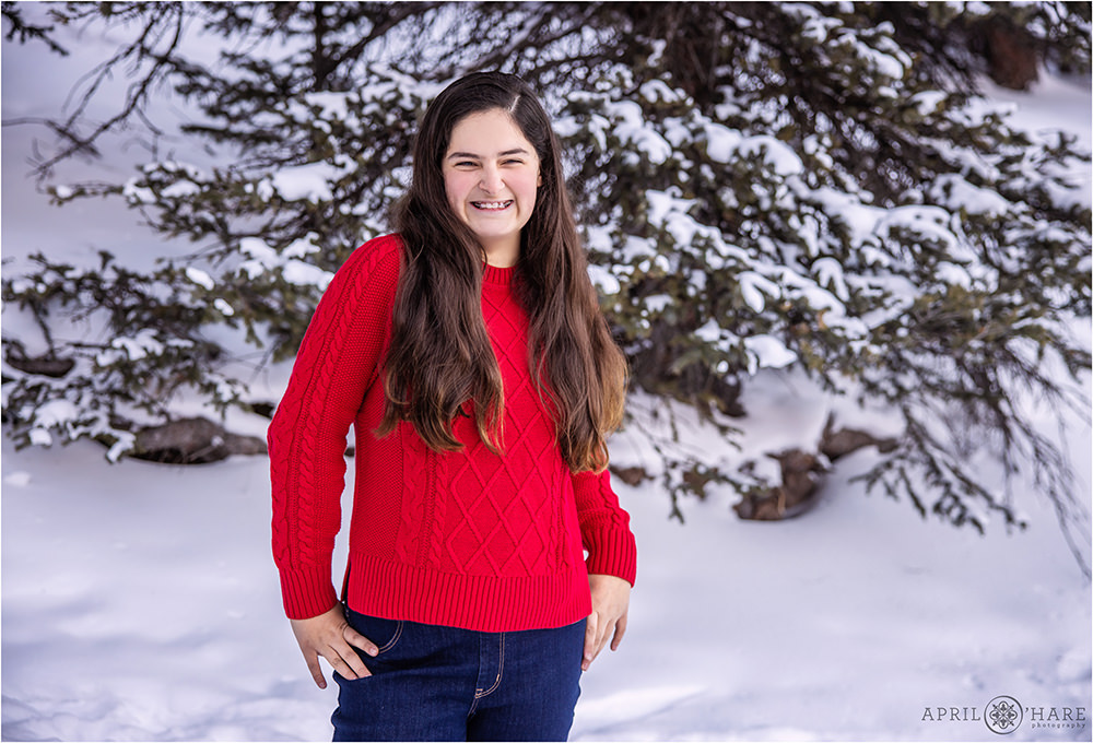Cute teenage girl wearing ared sweater at her family photoshoot in the woods during winter in Colorado