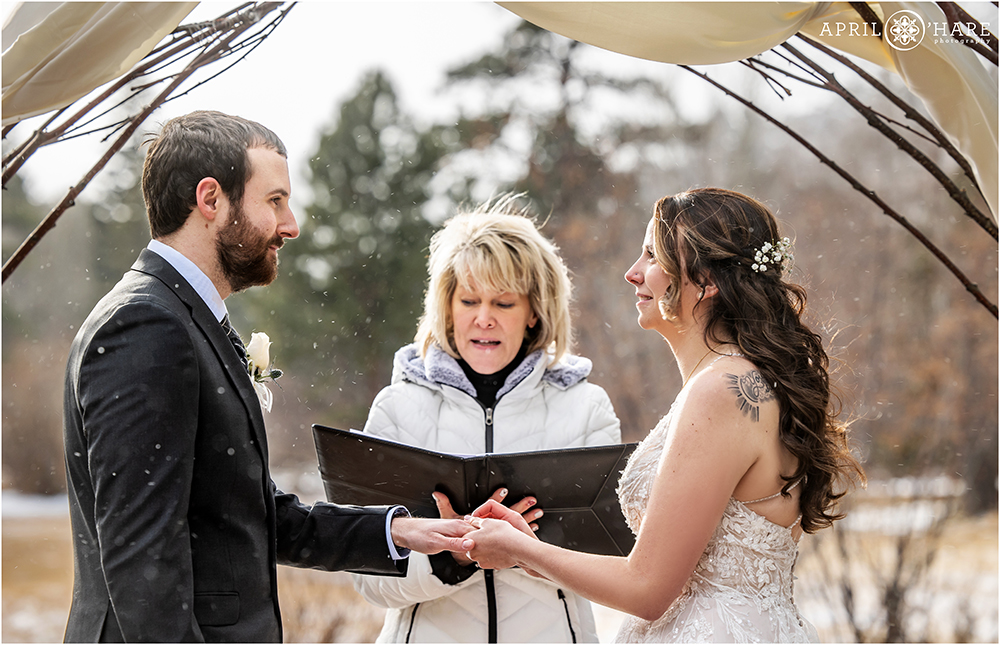 Bride and groom exchange rings at their outdoor snowy cold winter wedding at Romantic Riversong Inn in Estes Park Colorado