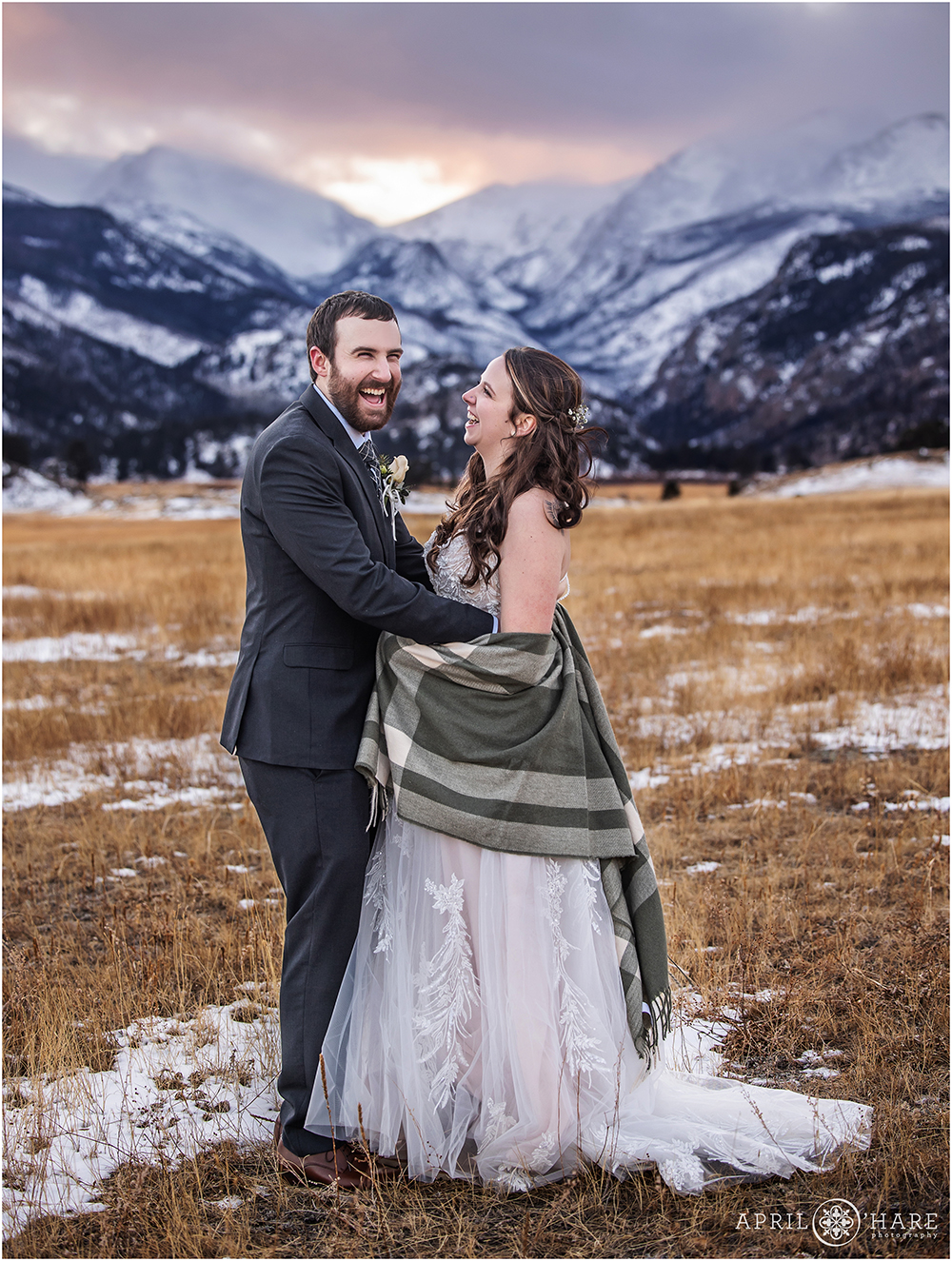 Groom cracks up with his bride as she looks at him in front of a gorgeous snowy mountain backdrop at sunset at RMNP