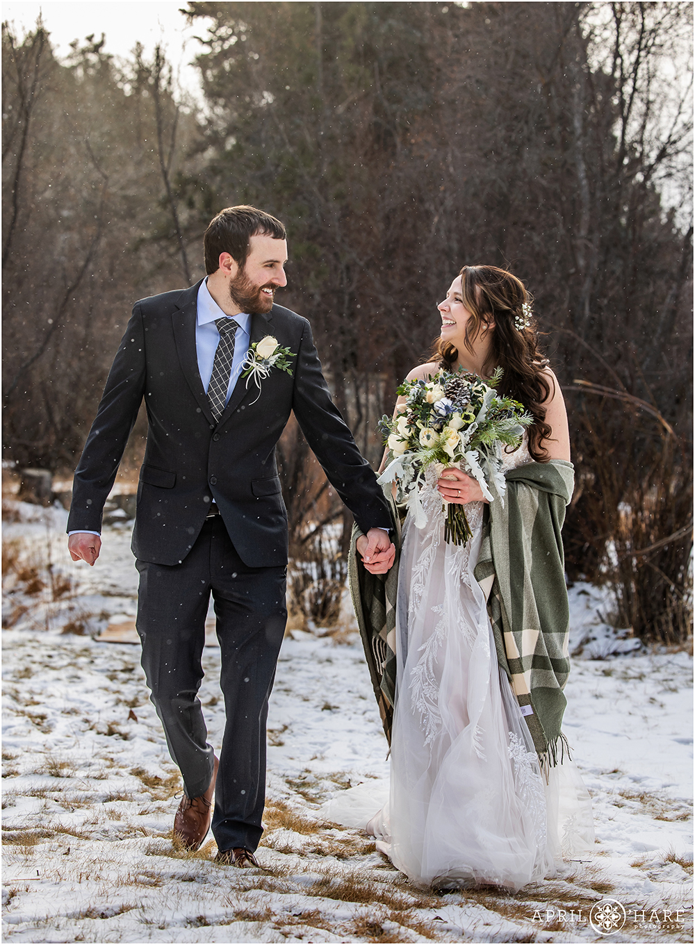 Chilly wedding day portrait of a couple walking through the snow together in Estes Park Colorado