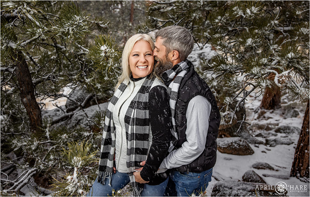Couple snuggles at their family portrait session surrounded by snow covered Evergreen trees in Colorado