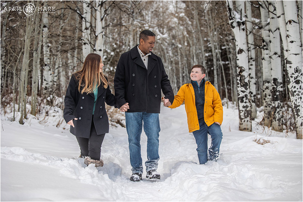 Family of three walk through a pretty snow covered aspen tree forest in Beaver Creek Colorado