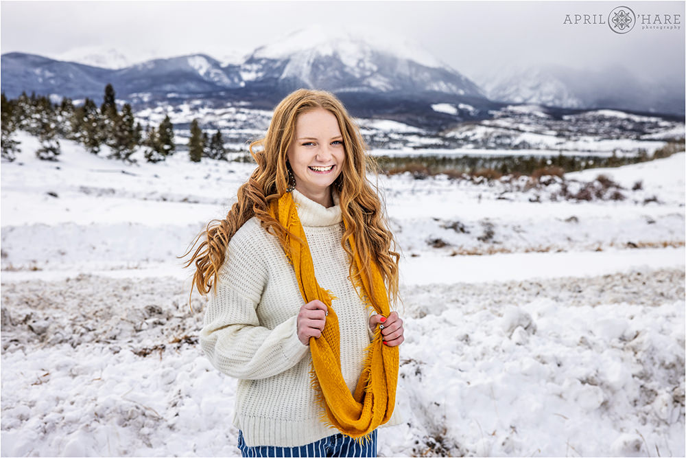 Teen girl wearing a yellow scarf and white sweater poses with a gorgeous mountain backdrop in Colorado