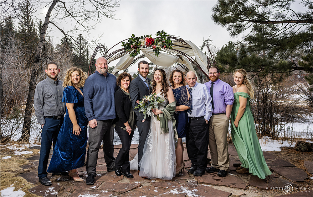 Large family portrait outside in front of a river and wood arch with florals on a cold December wedding day at Romantic Riversong Inn