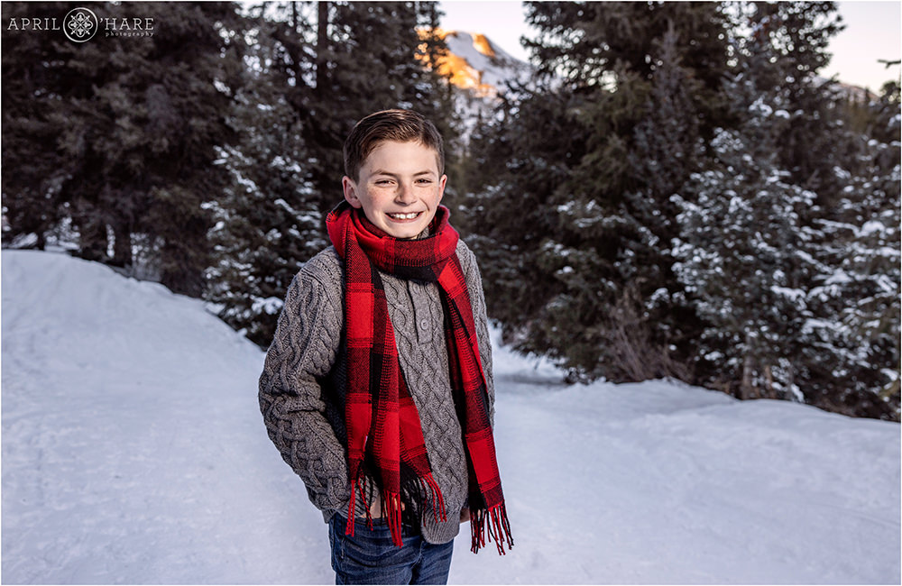 Young boy wearing a buffalo check red scarf and gray sweater poses in the woods at the Mayflower Gulch Trail in Colorado
