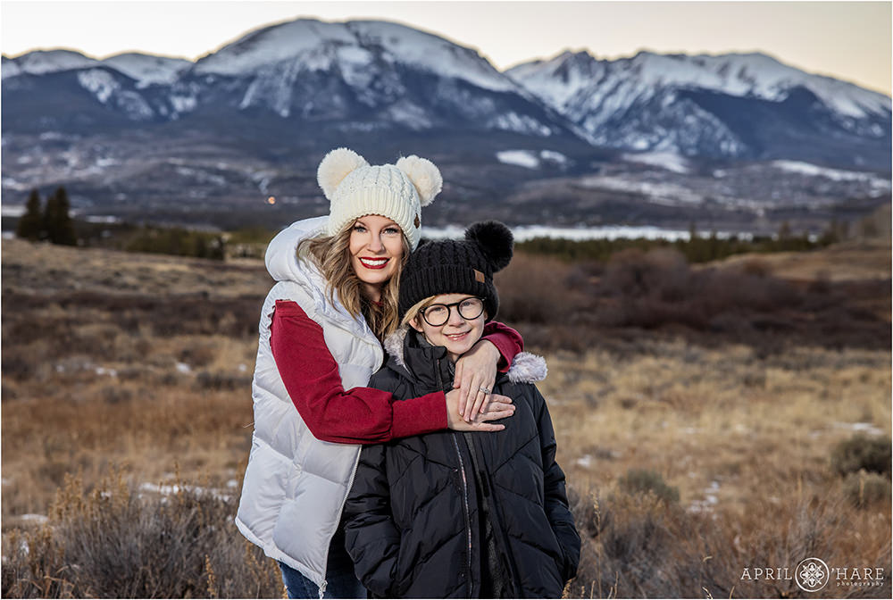 Mom hugs her son from behind in their matching pom hats during winter at Sapphire Point