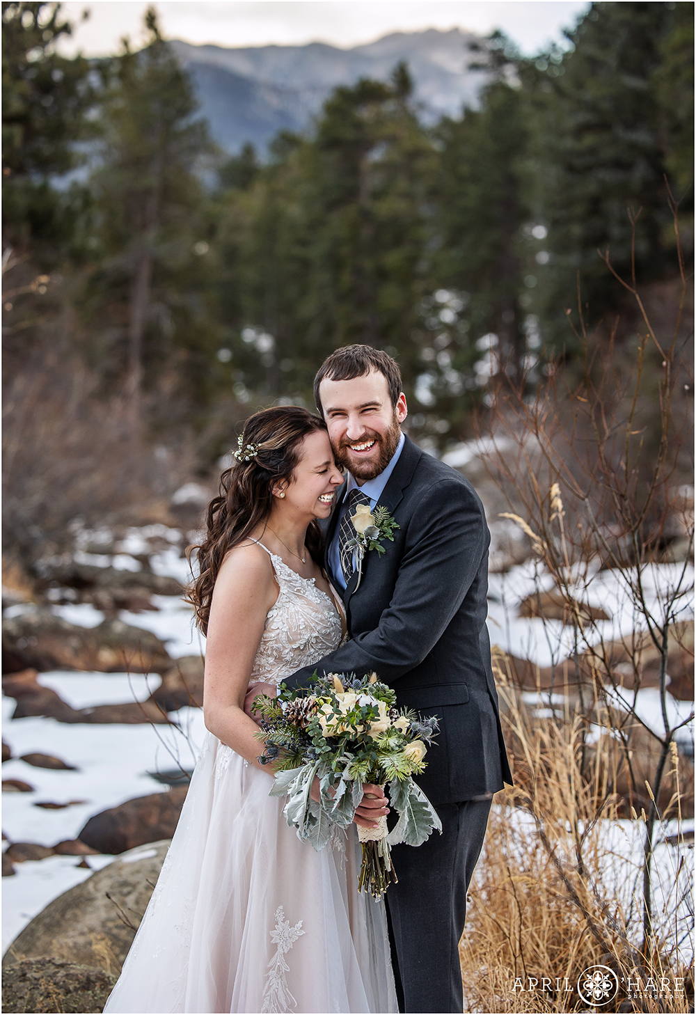 Candid natural wedding day portrait of a couple cracking up together in front of a beautiful icy river inside Rocky Mountain National Park
