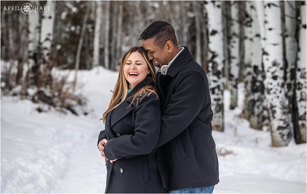 Cute couple laugh together in a gorgeous winter aspen tree forest setting near Beaver Creek Colorado