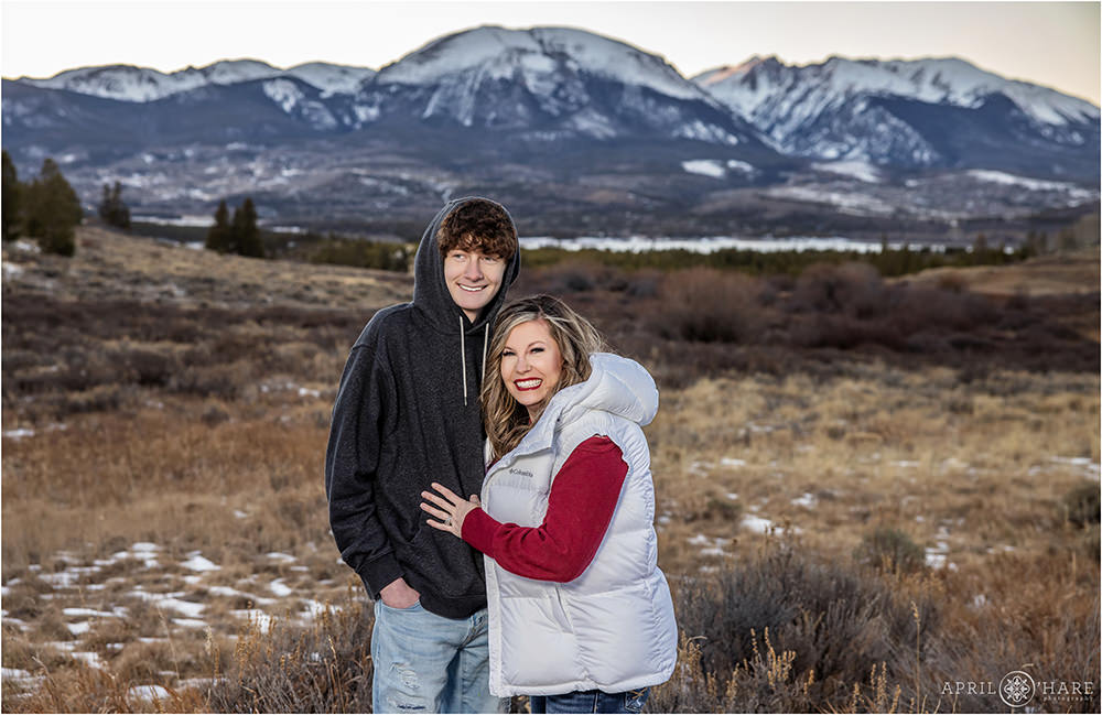 A teenage boy wearing a black hoodie laughs with his mom at their family photoshoot in the mountains of Colorado