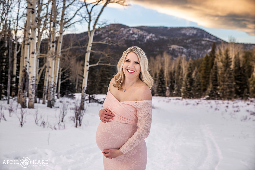 Beautiful blonde pregnant mama to be poses in a mountain forest during winter in Colorado