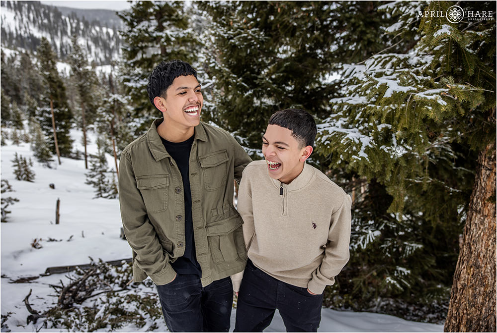 Two teenage brothers laugh at their family portraits in the snowy woods of Colorado