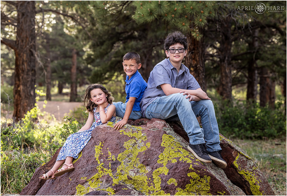3 kids sit on a cool rock covered with lichen at Shanahan Ridge Trailhead in Boulder CO