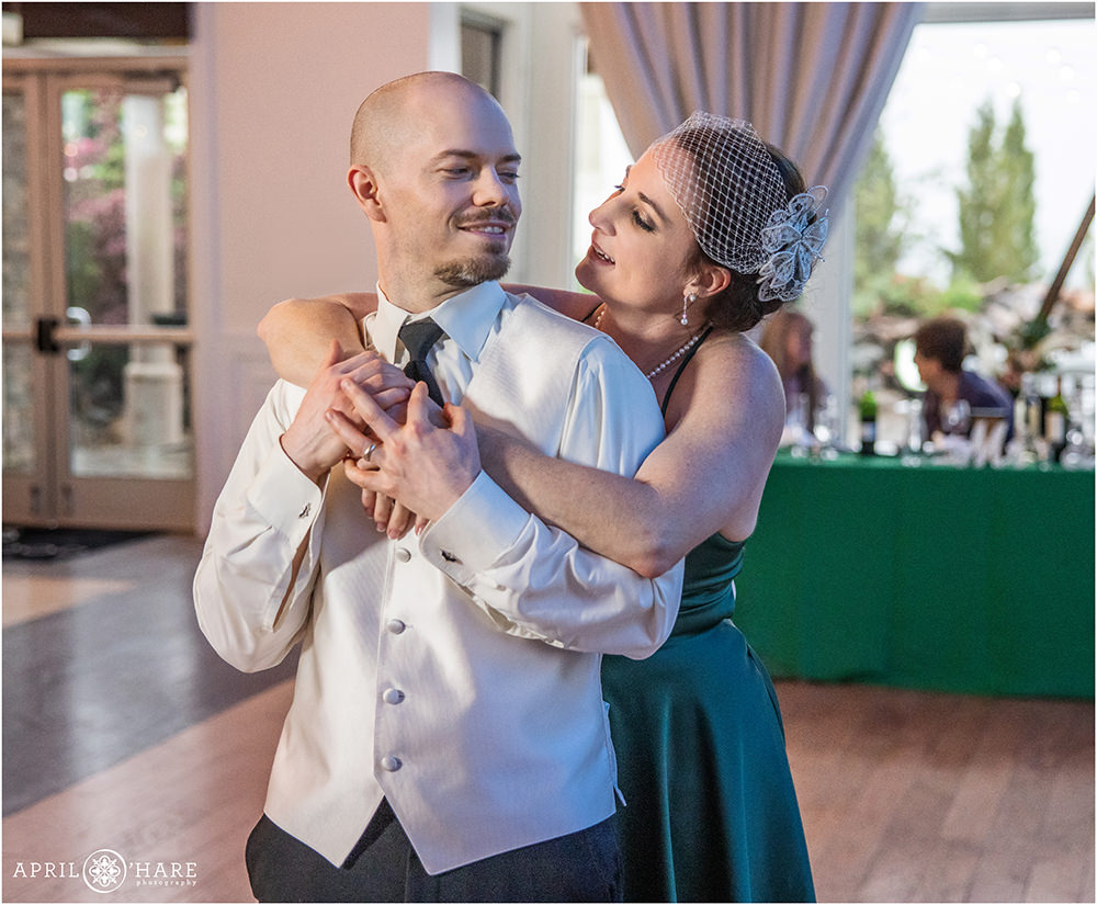 Married couple embrace on the dance floor with the wife wearing a birdcage bridal veil and a pretty green dress at their vow renewal party in Colorado