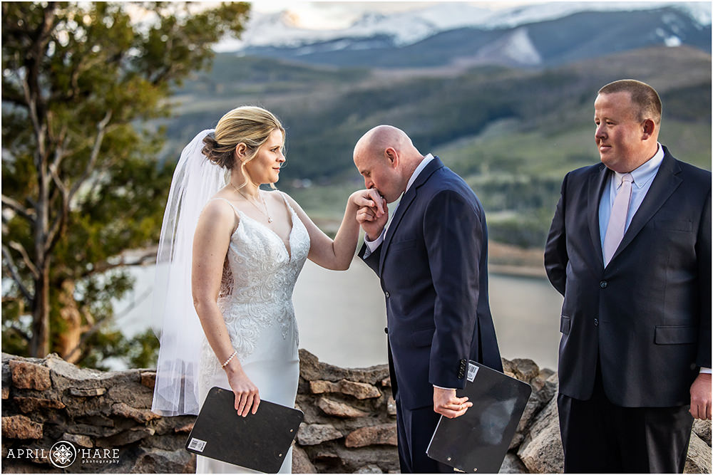 Groom kisses his bride's hand at their outdoor sunset wedding ceremony at Sapphire Point in Colorado